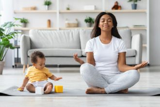 Mental Wellness Concept. Calm Happy Black Mother Meditating With Baby At Home